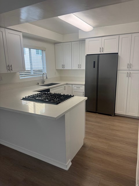 A kitchen with wood flooring, white cabinets and a black fridge.